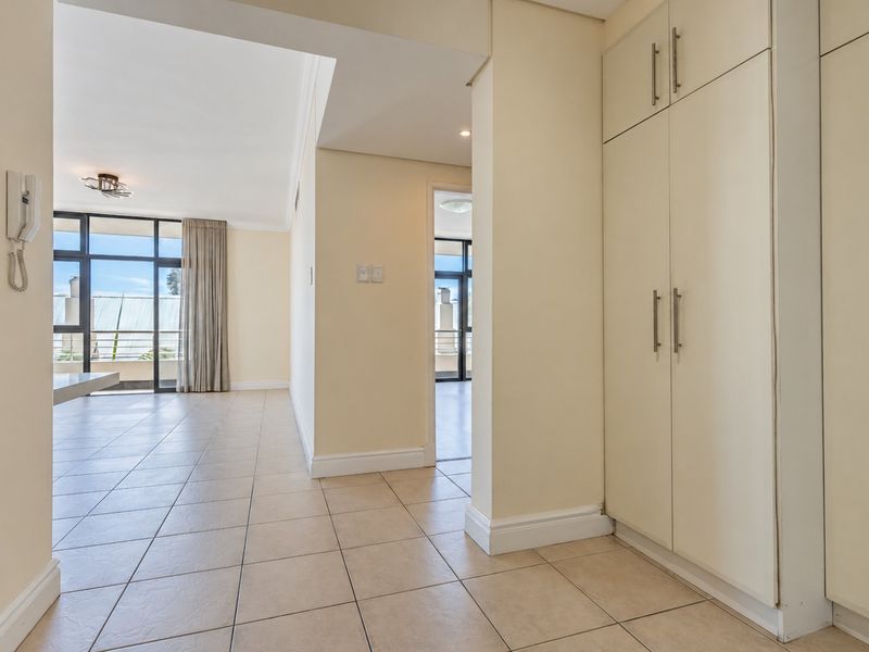 A bright and spacious hallway featuring neutral tiled flooring and ample built-in storage cupboards, leading into the open-plan living area.