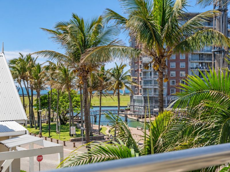 A scenic elevated view overlooking a landscaped park, waterway, pedestrian bridge, and surrounding apartment buildings.