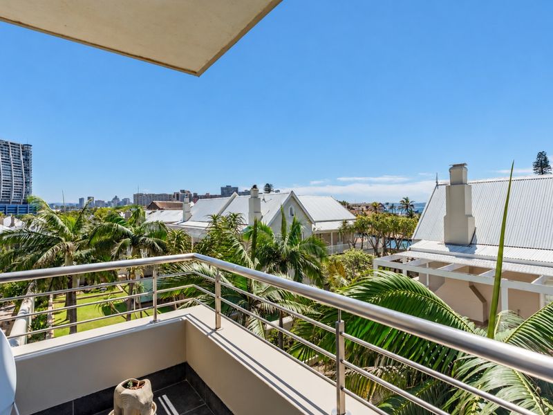 A spacious balcony featuring a modern stainless steel balustrade and tiled flooring, offering elevated views of the surrounding neighborhood and palm trees.