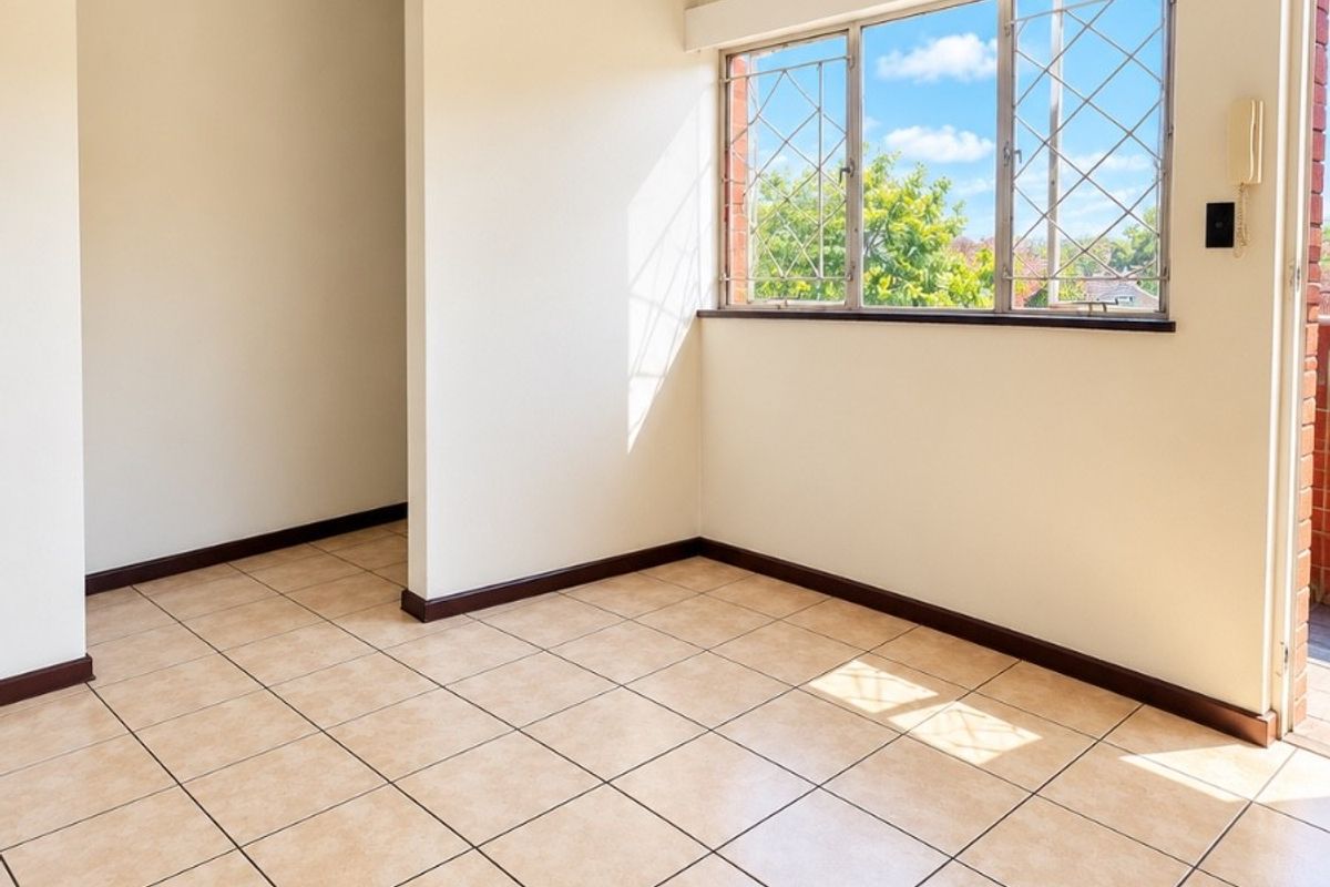 A bright, empty living area featuring neutral ceramic floor tiles, security-barred windows, and an intercom system, offering a clean canvas for interior design.