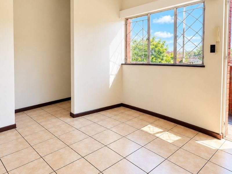 A bright, empty living area featuring neutral ceramic floor tiles, security-barred windows, and an intercom system, offering a clean canvas for interior design.