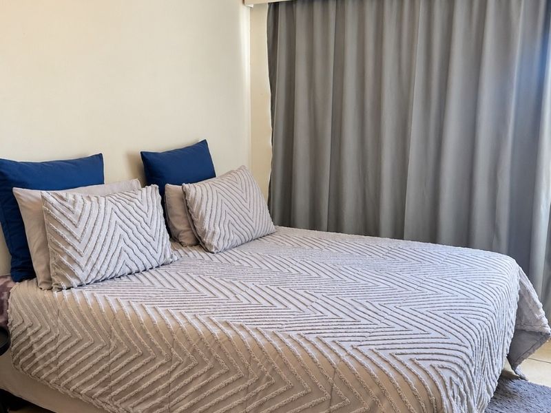 A bedroom featuring tiled flooring and a ventilation grille, with neutral wall finishes and a curtain track installed above the window area.