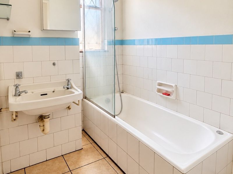 A functional bathroom featuring a wall-mounted basin, a bathtub with a glass shower screen, and classic white tiling with a blue accent border.