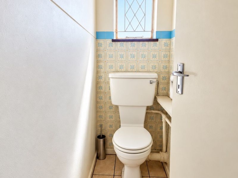 A compact, functional guest toilet featuring decorative wall tiling, tiled flooring, and a small window for natural light and ventilation.