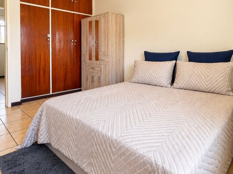 A bedroom featuring tiled flooring and built-in wooden cupboards, offering a functional and neutral space ready for personalization.