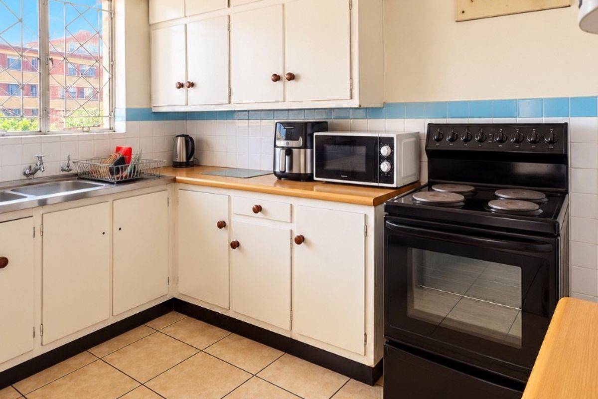 A functional kitchen featuring built-in cabinetry, a stainless steel sink, tiled splashback, and a freestanding electric stove with a visible electrical distribution board.