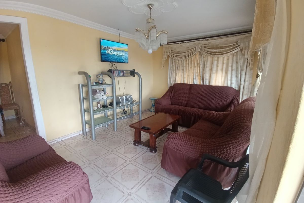 A living room featuring tiled flooring, decorative ceiling rose with a chandelier, and classic cornicing, offering a functional space for relaxation.