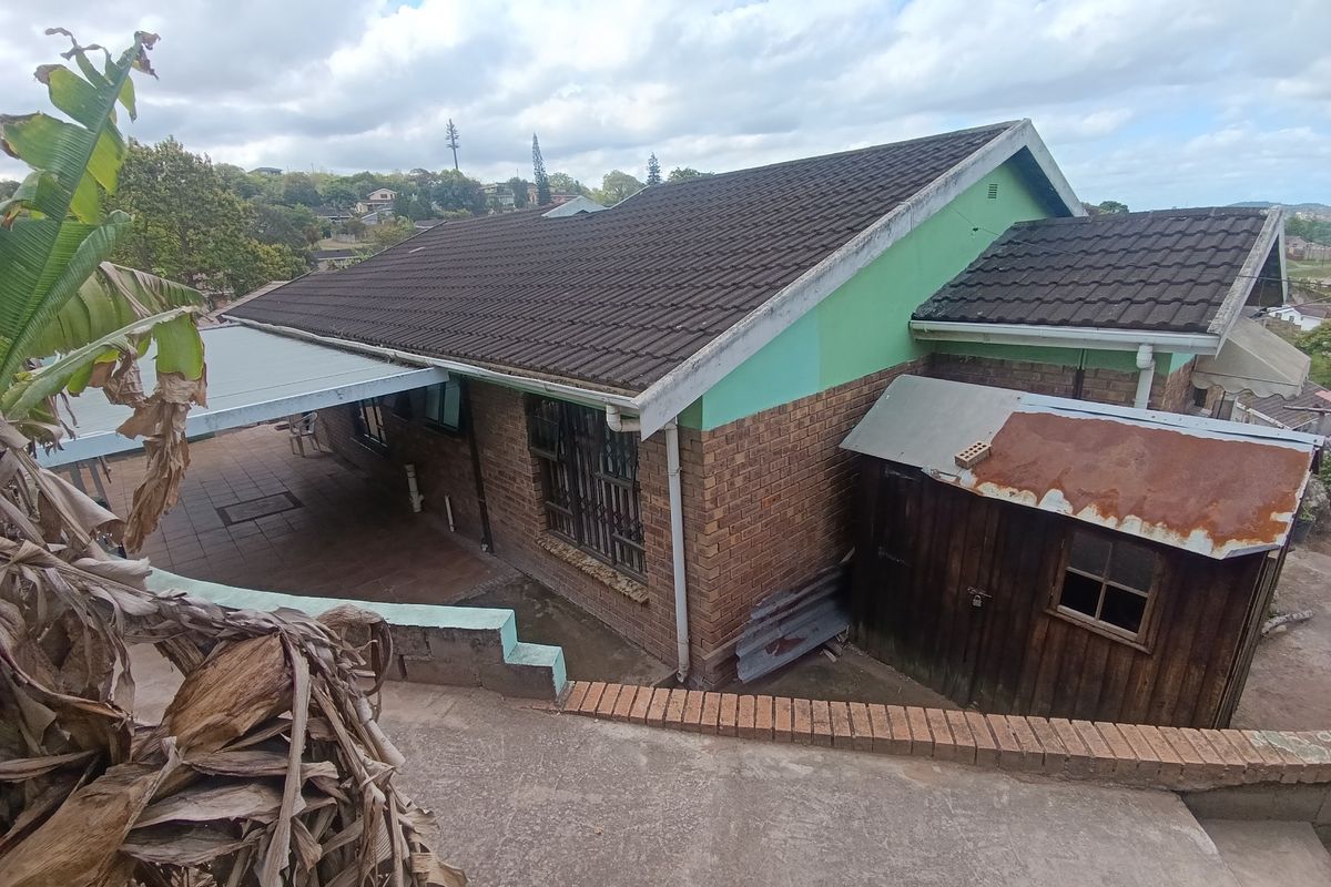 Rear view of the property featuring a brick facade, tiled roof, covered patio area, and a detached timber shed with a rusted roof.