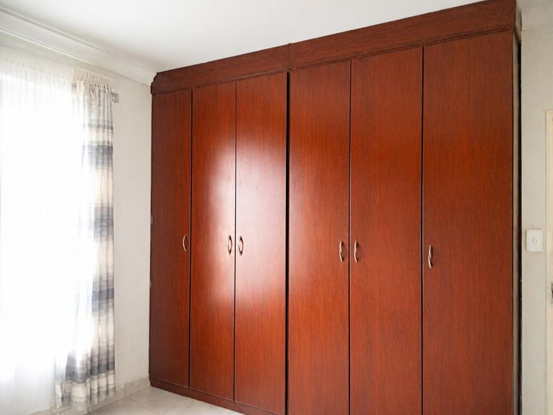A bedroom featuring a large, floor-to-ceiling built-in wooden wardrobe with ample storage space and neutral tiled flooring.