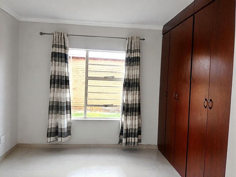 A bright, empty bedroom featuring tiled flooring and floor-to-ceiling built-in wooden cupboards, offering a clean and neutral space ready for personalization.