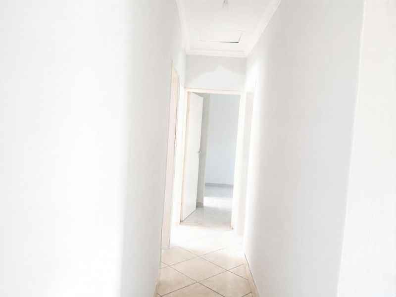 A bright, empty hallway featuring tiled flooring and a ceiling access hatch, providing access to adjacent rooms.