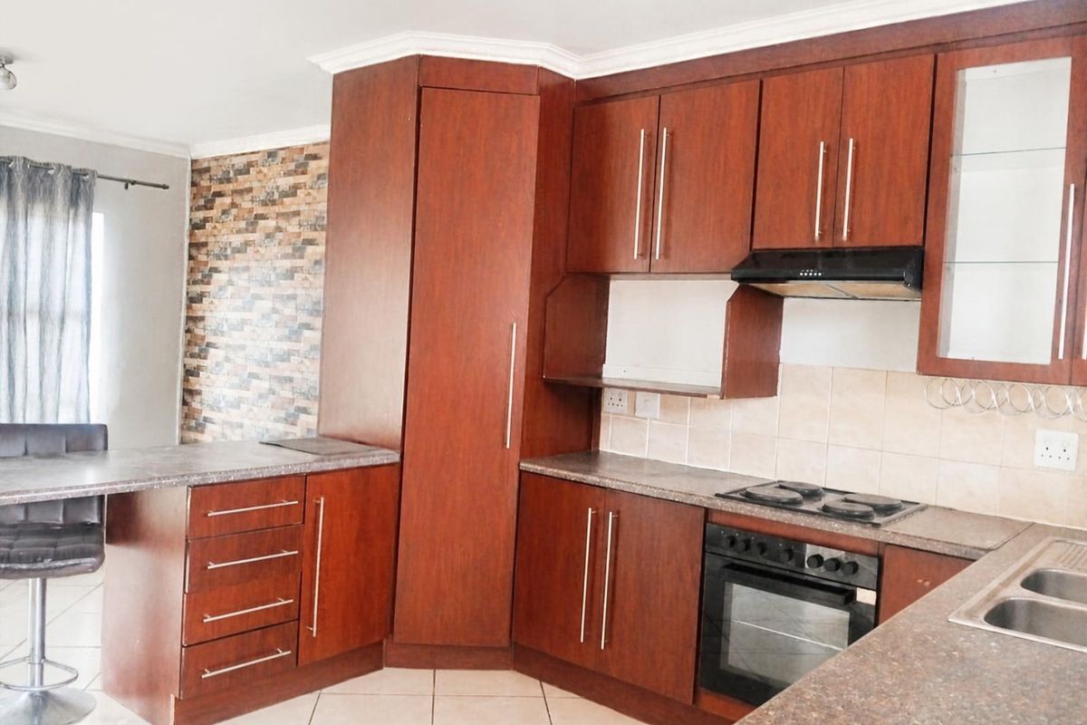 A functional kitchen featuring dark wood cabinetry, laminate countertops, built-in oven, electric hob, and a tiled backsplash with a breakfast nook area.