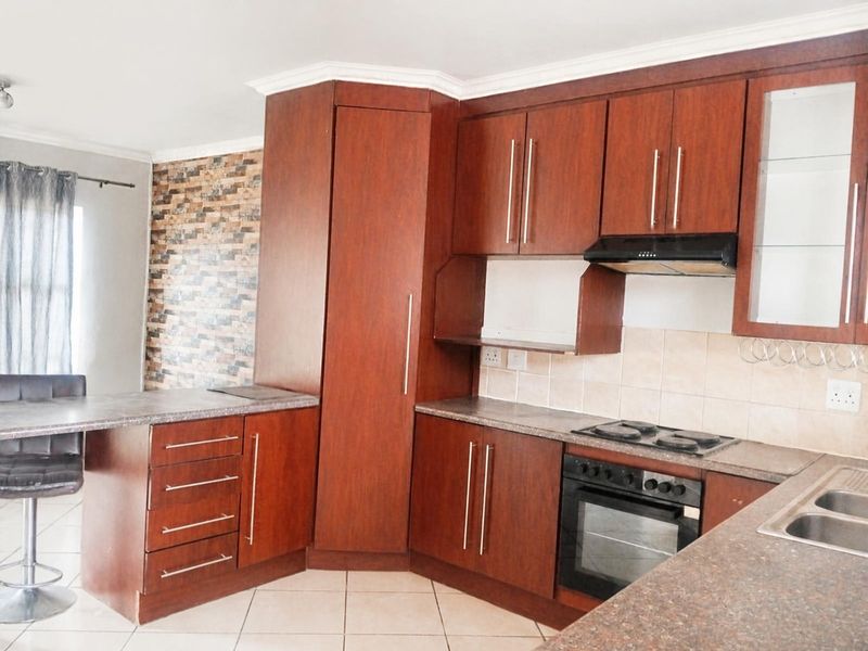 A functional kitchen featuring dark wood cabinetry, laminate countertops, built-in oven, electric hob, and a tiled backsplash with a breakfast nook area.