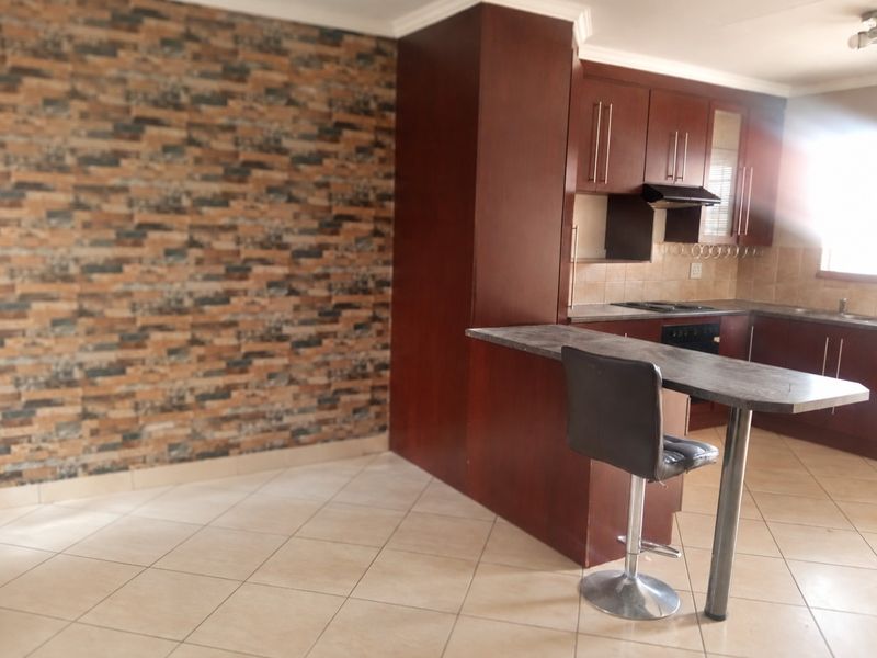 A functional kitchen featuring dark wood cabinetry, a breakfast bar, built-in oven and hob, and a decorative stone-cladding feature wall.