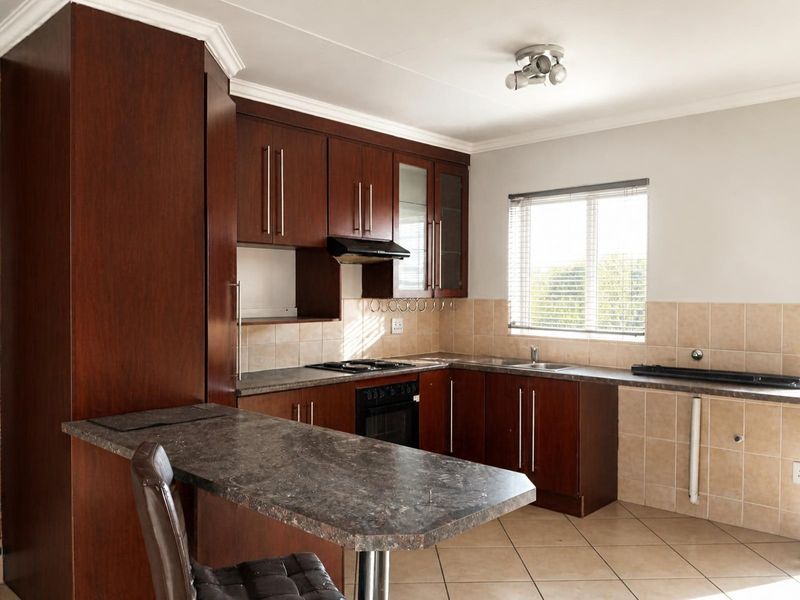 Functional kitchen featuring dark wood cabinetry, laminate countertops, built-in oven, hob, extractor fan, and a breakfast bar with tiled flooring and backsplash.