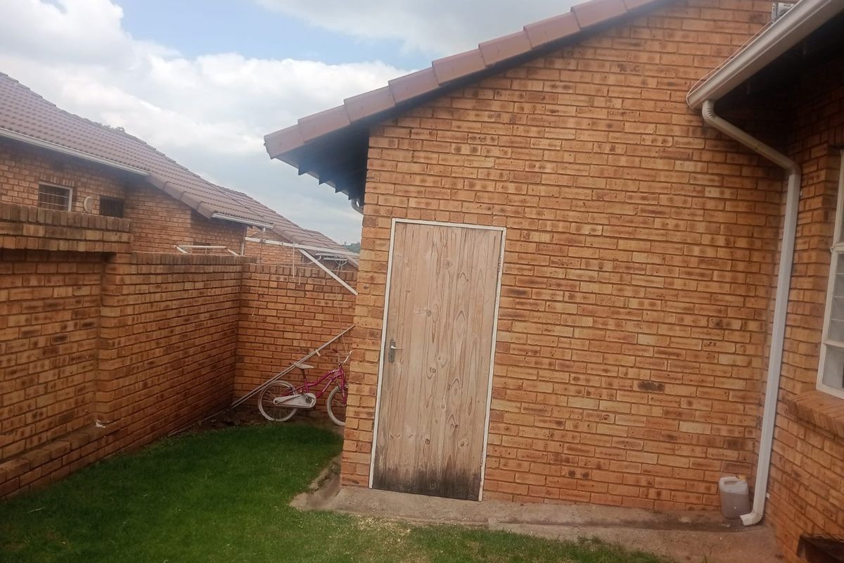 Rear exterior view of the townhouse featuring face-brick walls, tiled roofing, and a side access door leading to the garden area.