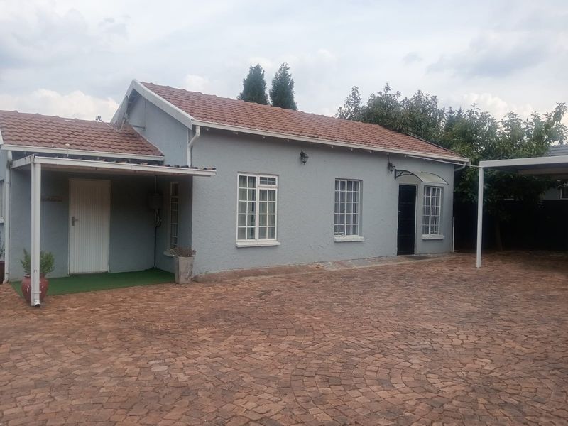 Front exterior view of a single-story house featuring a tiled roof, paved driveway, and covered parking area.