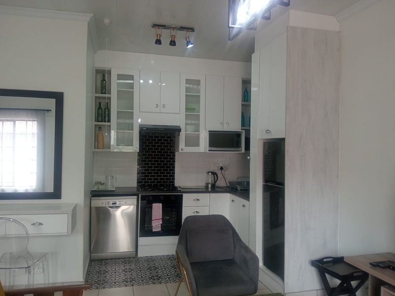 A compact, modern kitchen featuring white cabinetry, a black subway tile backsplash, integrated appliances, and decorative patterned floor tiles.