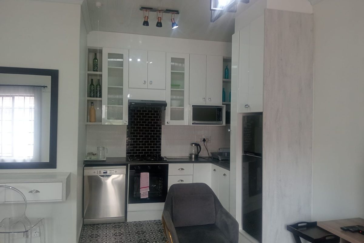 A compact, modern kitchen featuring white cabinetry, a black subway tile backsplash, integrated appliances, and decorative patterned floor tiles.
