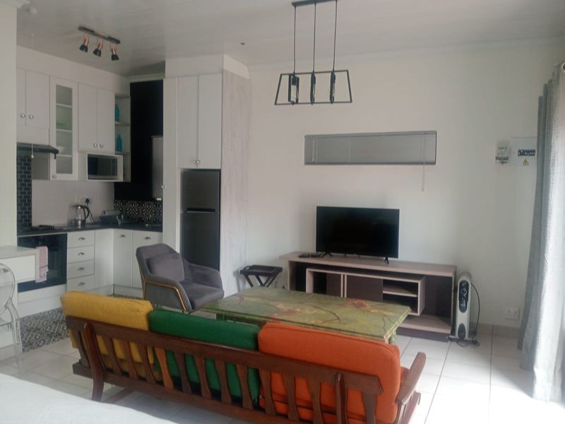 Open-plan living area featuring a modern kitchen with built-in cabinetry, oven, and extractor fan, seamlessly flowing into a tiled lounge space.