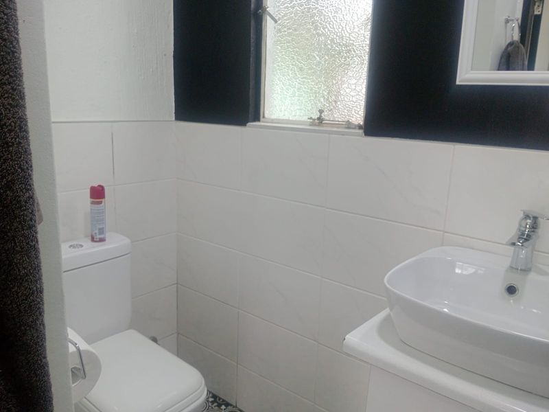A compact bathroom featuring a modern vessel basin on a vanity, a standard toilet, and white wall tiling with a small obscured glass window.