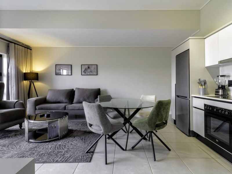 A modern open-plan living and kitchen area featuring sleek cabinetry, integrated appliances, and neutral tiled flooring, creating a cohesive and functional living space.