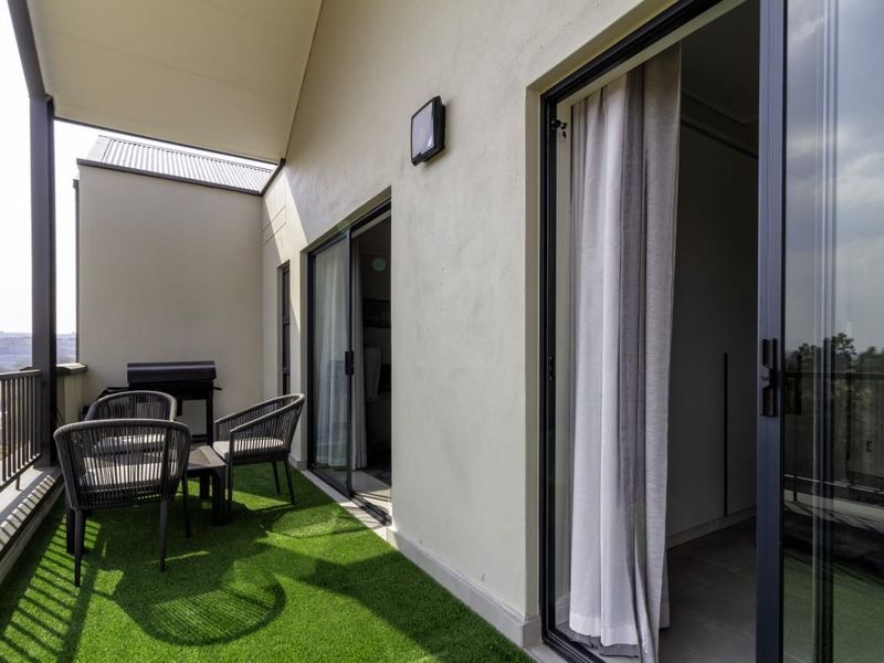 A covered balcony featuring artificial grass flooring, metal railings, and sliding glass door access to the interior living space.