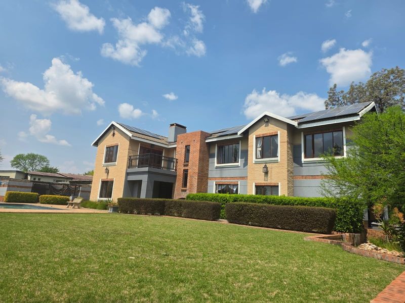 A spacious rear exterior view of a two-story house featuring a large lawn, swimming pool, balcony, and solar panel installation on the roof.