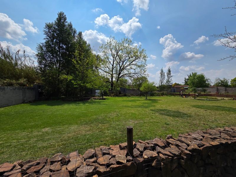 A spacious, well-maintained garden featuring a large lawn, mature trees, and a decorative stone boundary wall.