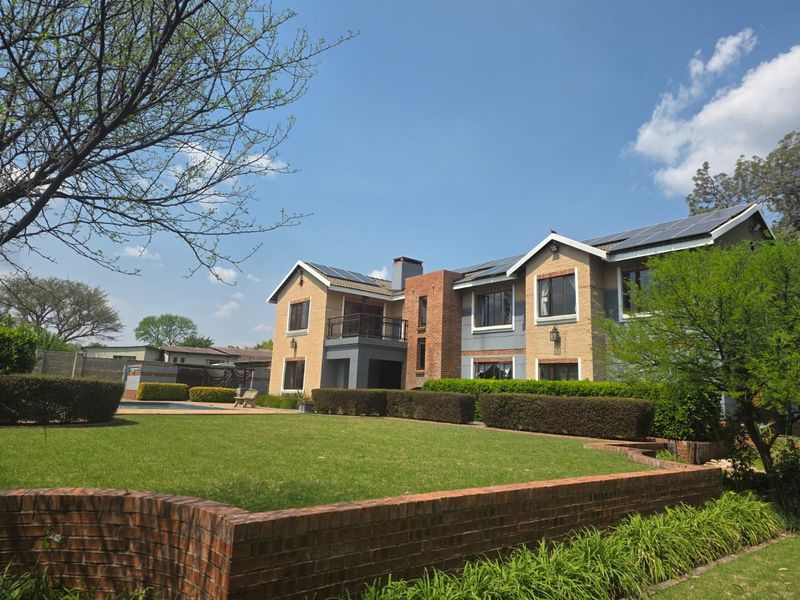 Rear view of a multi-story residential property featuring a brick facade, solar panels, a balcony, and a well-maintained garden with a swimming pool.
