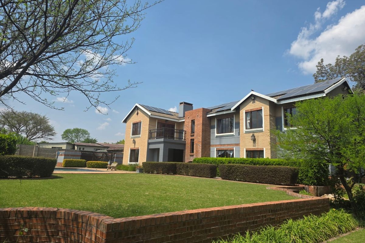 Rear view of a multi-story residential property featuring a brick facade, solar panels, a balcony, and a well-maintained garden with a swimming pool.