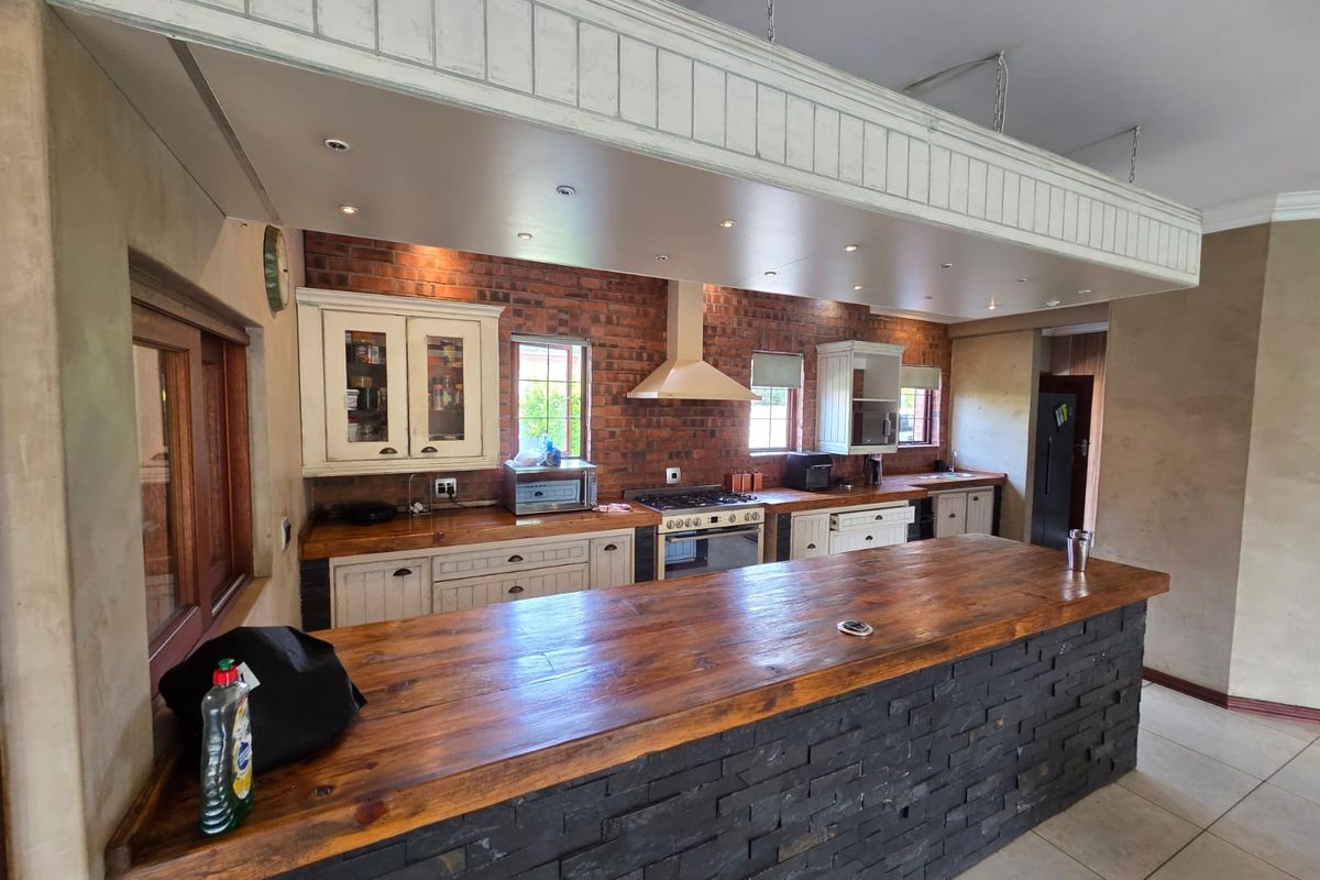 Spacious kitchen featuring a large wooden island, exposed brick walls, built-in oven with gas hob, and ample cabinetry with recessed ceiling lighting.