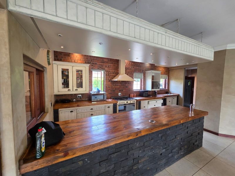 Spacious kitchen featuring a large wooden island, exposed brick walls, built-in oven with gas hob, and ample cabinetry with recessed ceiling lighting.