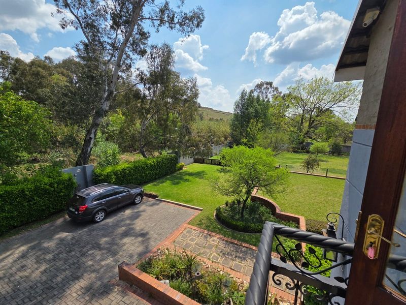 Elevated view overlooking a well-maintained garden, paved driveway, and lush green surroundings from a private balcony.