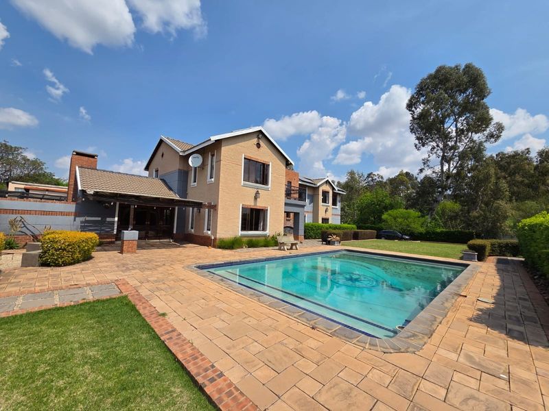 A spacious rear garden featuring a swimming pool, paved patio area, and a covered outdoor entertainment space attached to the main house.