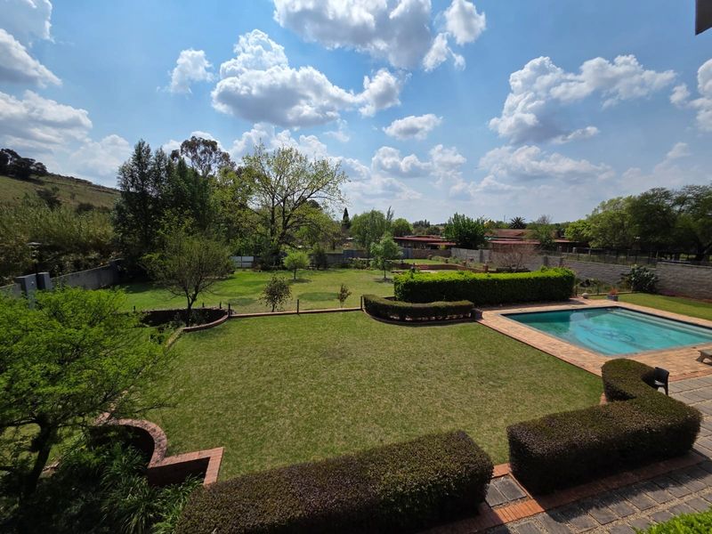 Spacious outdoor area featuring a well-maintained swimming pool, expansive lawn, manicured hedging, and established garden surroundings.