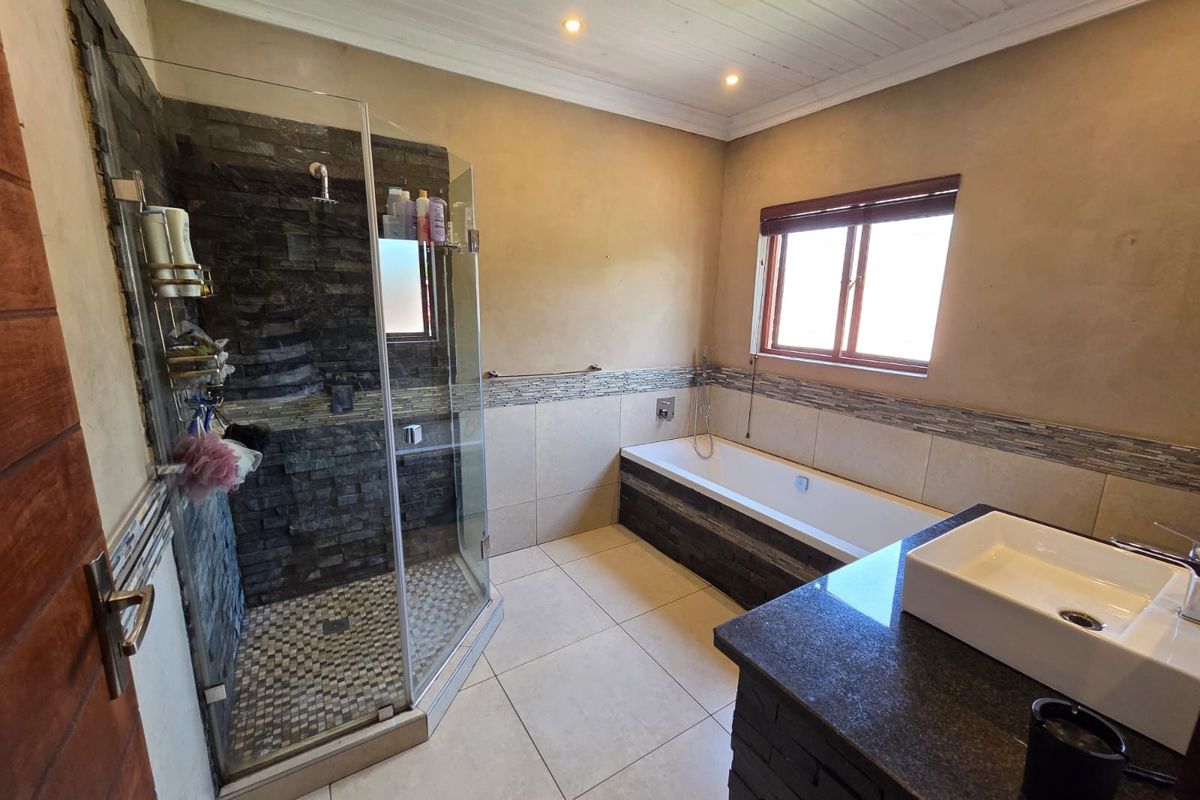 A well-appointed bathroom featuring a glass-enclosed shower with stone cladding, a built-in bathtub, and a modern vessel sink set on a granite vanity.