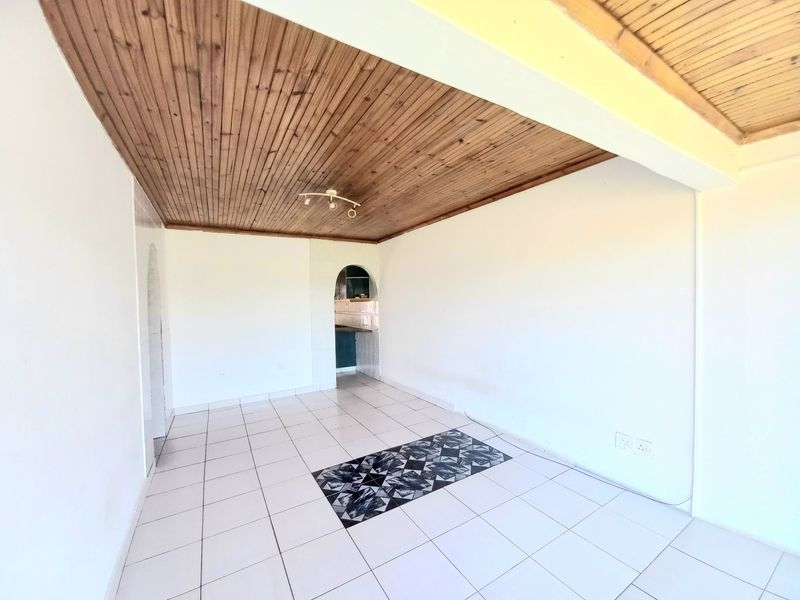 An empty living area featuring white walls, ceramic floor tiles, and a distinctive timber tongue and groove ceiling with an arched entryway.