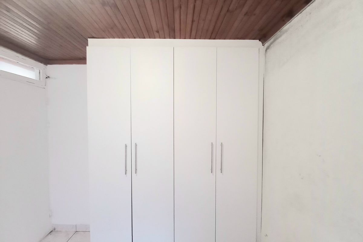A bedroom featuring a built-in wardrobe, timber ceiling, and tiled flooring, showing signs of wall staining requiring maintenance.
