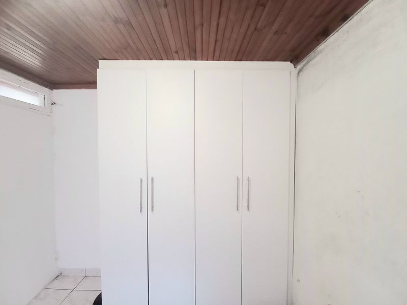 A bedroom featuring a built-in wardrobe, timber ceiling, and tiled flooring, showing signs of wall staining requiring maintenance.