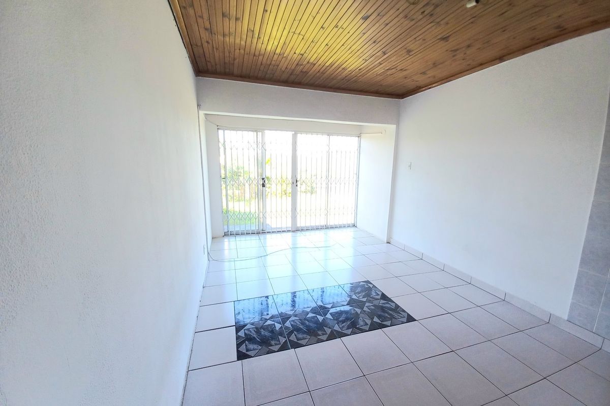 An empty living room featuring a timber ceiling, ceramic tiled flooring with a decorative inlay, and a sliding glass door with a security gate.