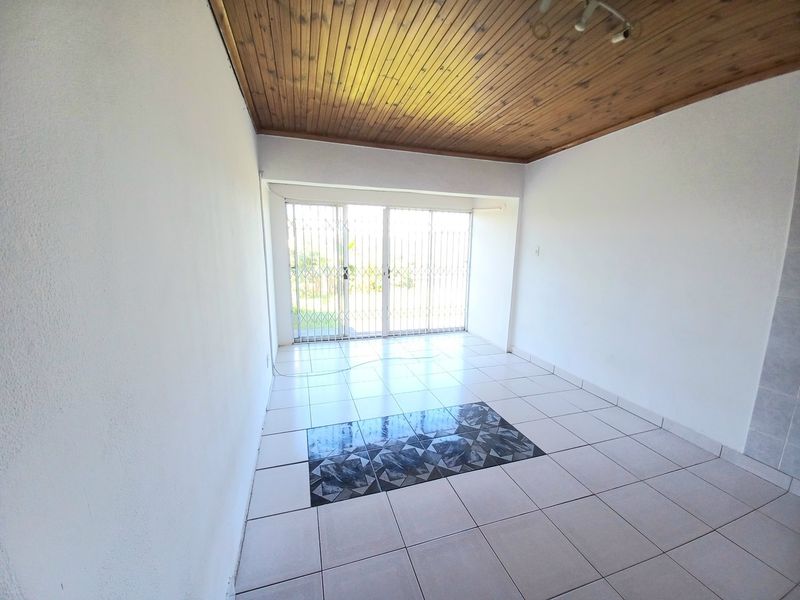 An empty living room featuring a timber ceiling, ceramic tiled flooring with a decorative inlay, and a sliding glass door with a security gate.