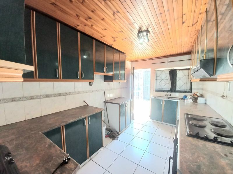 A functional kitchen featuring built-in cabinetry, laminate countertops, an electric hob, and tiled flooring, with a timber ceiling and direct access to the exterior.