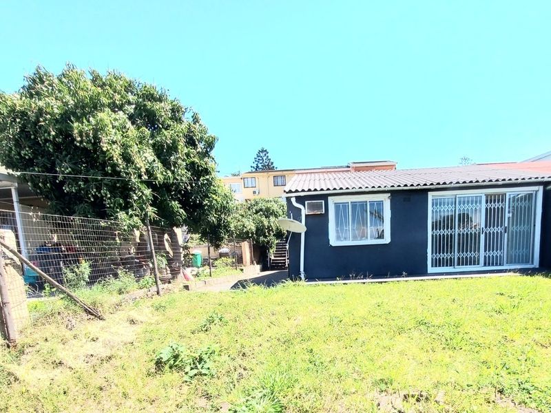 Rear view of the property featuring a dark-painted exterior, sliding glass doors with security gates, and a large backyard area with boundary fencing.