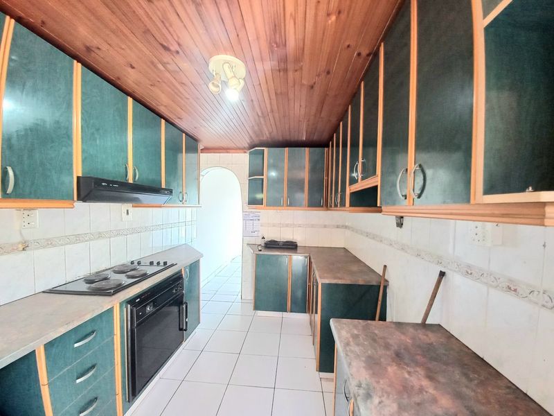 A dated kitchen featuring dark green cabinetry, timber ceiling, tiled flooring, and built-in cooking appliances, offering significant potential for a modern renovation.