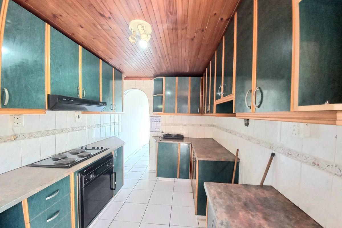 A dated kitchen featuring dark green cabinetry, timber ceiling, tiled flooring, and built-in cooking appliances, offering significant potential for a modern renovation.