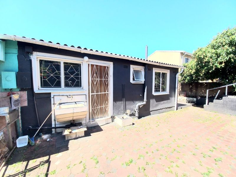 Rear exterior view of the property featuring a paved patio area, external wash basin, and security gates on the windows and door.