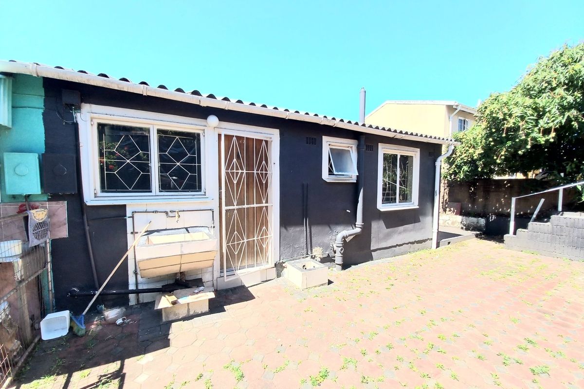 Rear exterior view of the property featuring a paved patio area, external wash basin, and security gates on the windows and door.