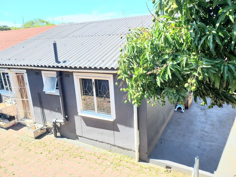Rear exterior view of the property featuring a corrugated metal roof, security bars on windows, and a paved outdoor area with an external sink.