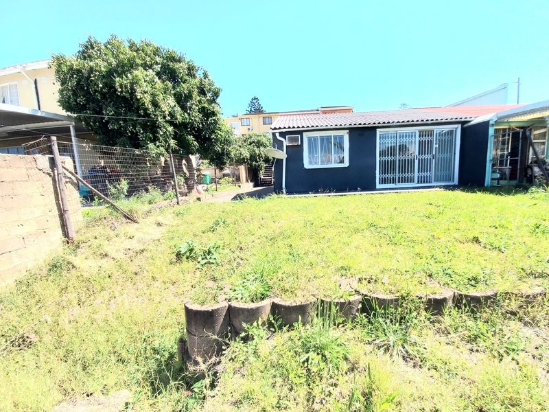Rear view of the property featuring a lawn area, concrete block retaining wall, and a sliding door with security gate access.